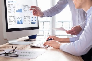 Pair of consultants analysing financial data displayed on a computer screen with business charts, fintech