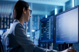 Female IT engineer working at desk with multiple computer screens