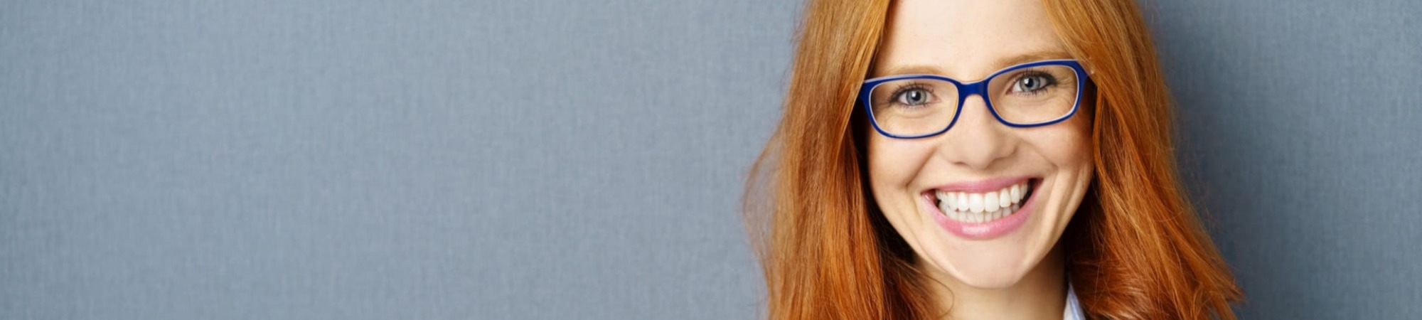 Portrait of young red-haired woman wearing glasses against grey background
